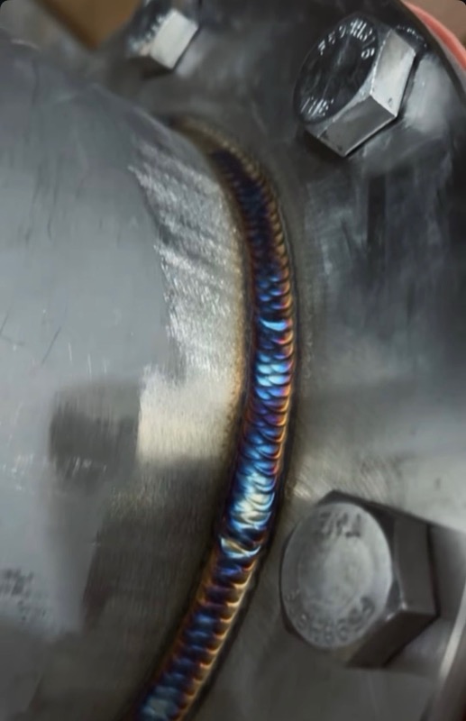 TIG weld cap with blue and gold peacock heat tint running around a bolted stainless flange